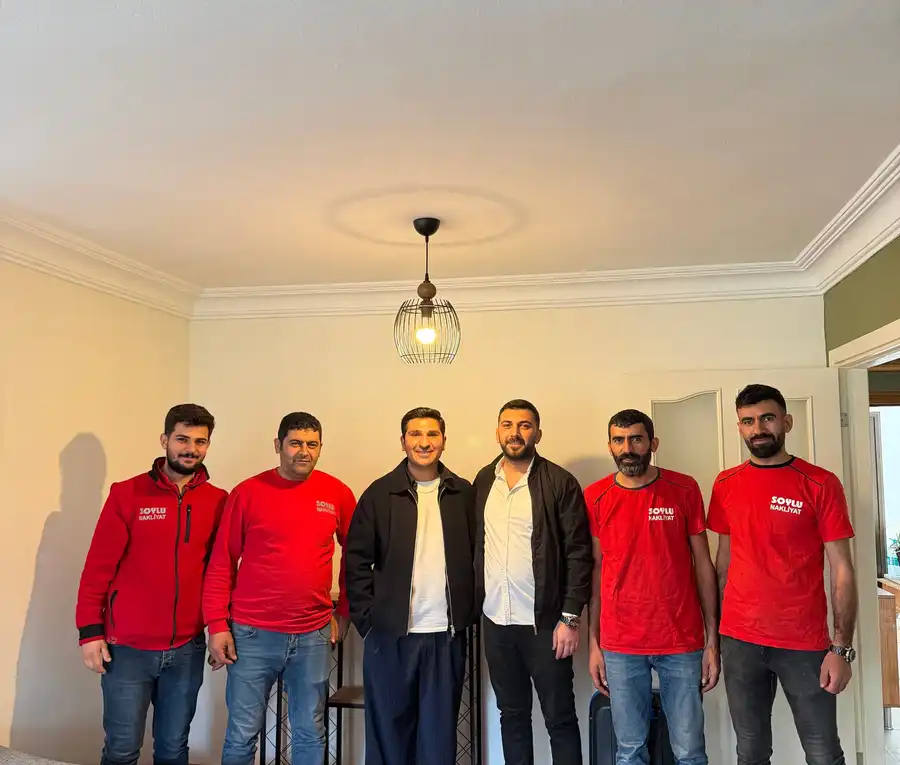 Yerleşimi biten bir salonda yan yana duran kırmızı kıyafetli Soylu ekibi ve iki kişi, önde koltuk ve sehpa
