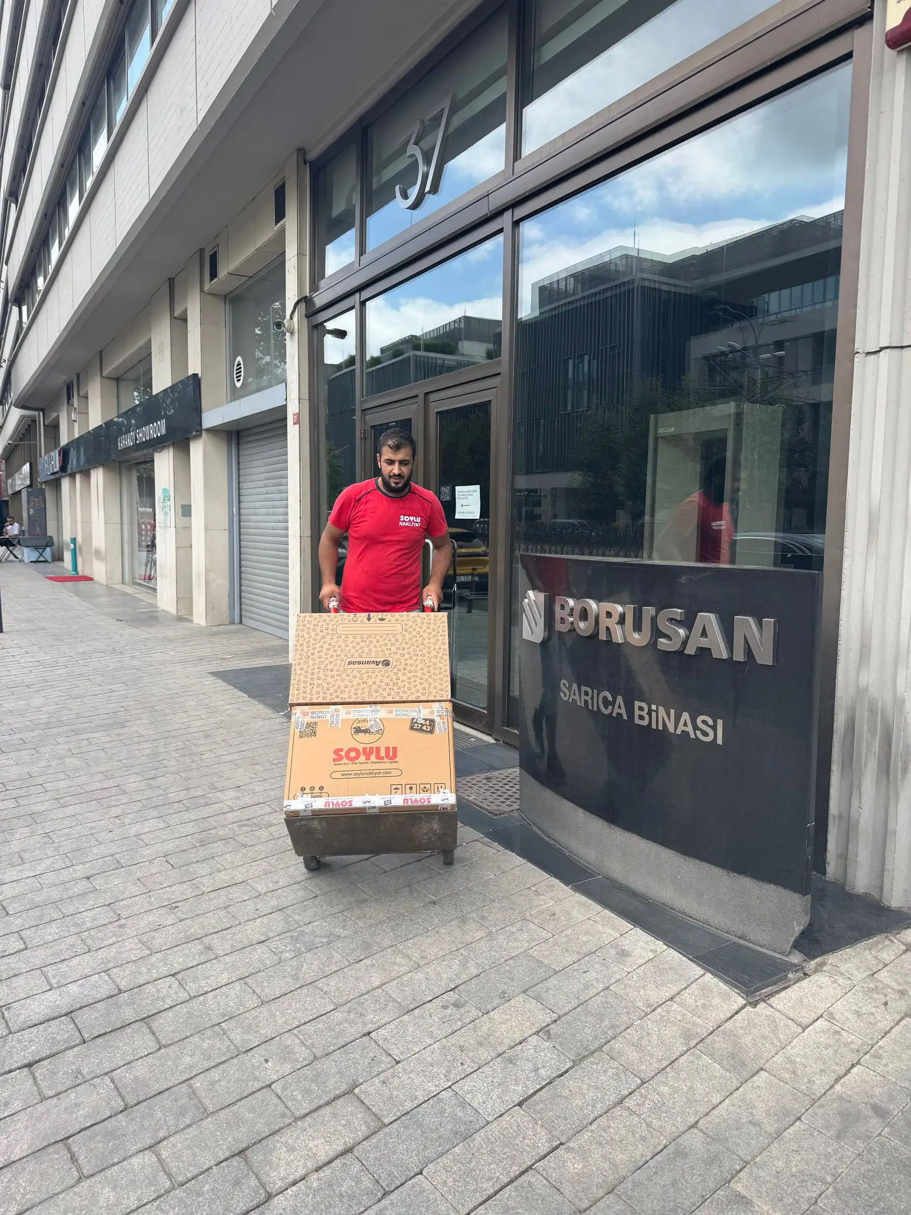 Soylu personeli koli arabasıyla ofis binasının cam girişinden koli taşıyor