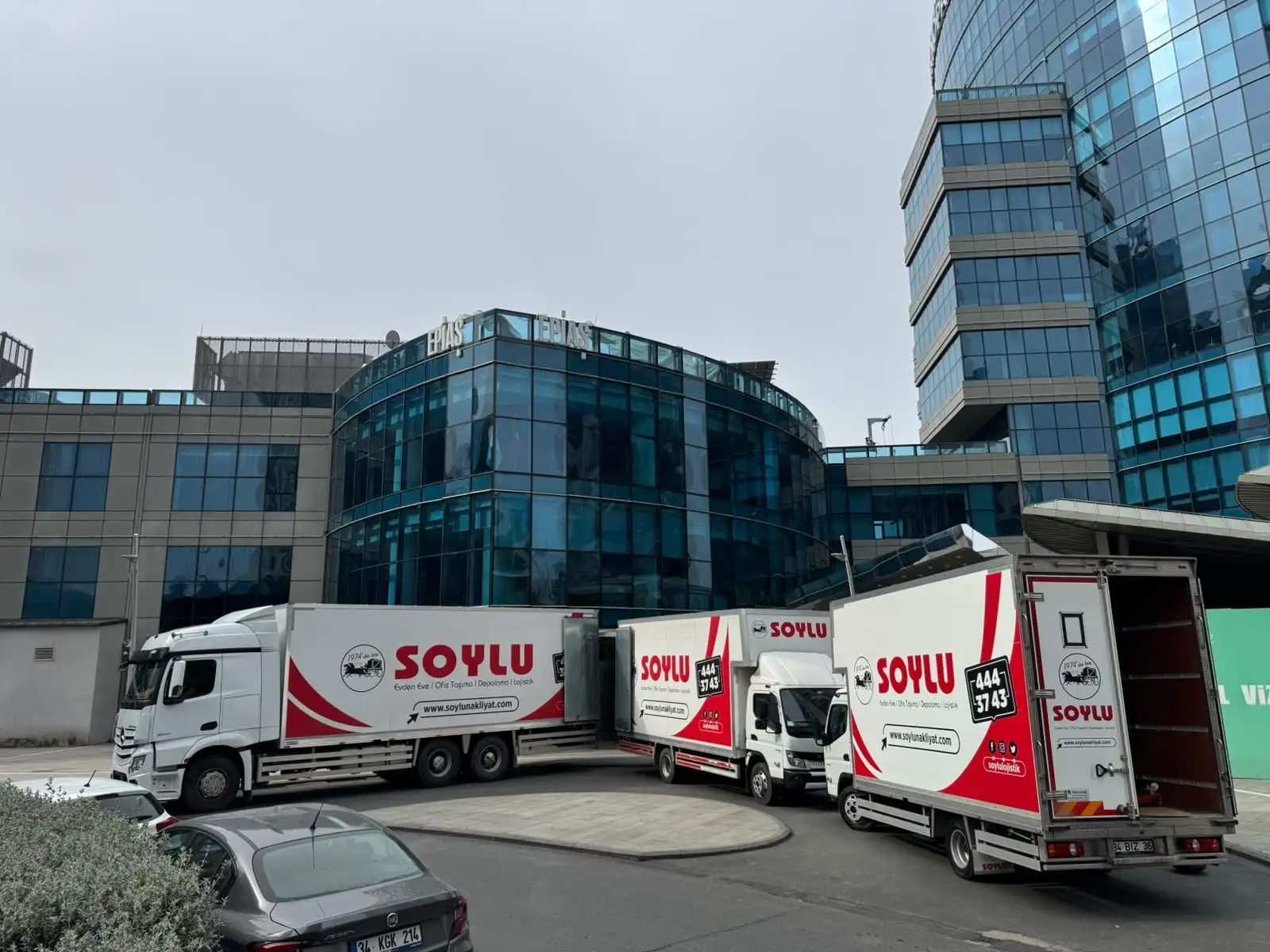 Soylu kamyonları cam cepheli ofis kompleksinin önünde kapıları açık yükleme yaparken
