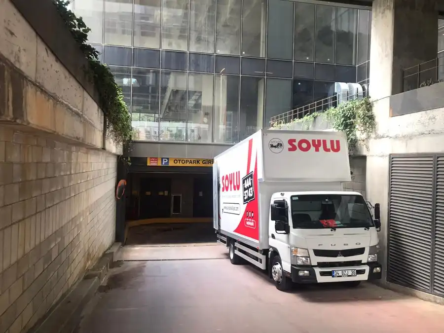 Cam cepheli bir iş binasının yer altı otopark girişi rampasında bekleyen beyaz Soylu kamyonu