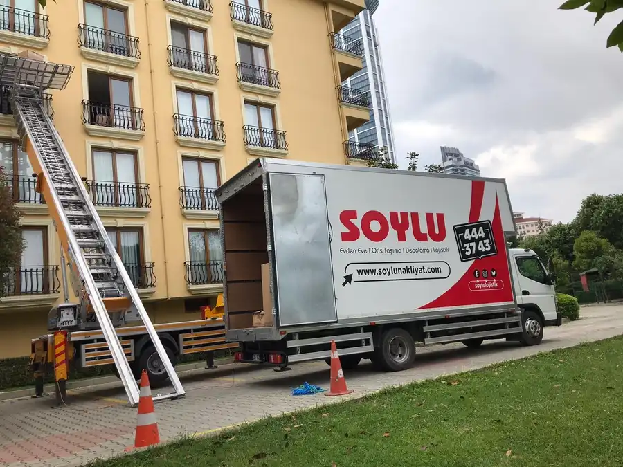 Sarı cepheli apartmanın önüne kurulmuş dış cephe asansörü ve kasası açık Soylu kamyonu