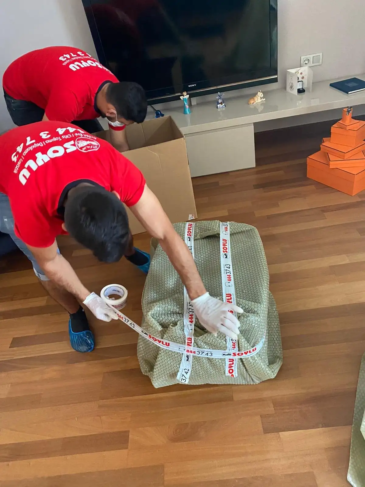 Soylu personeli eşyayı koruma örtüsüyle paketleyip bantlıyor