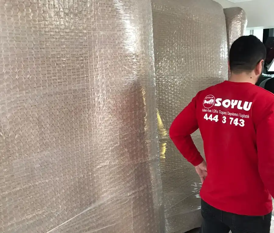 Balonlu naylon ve streçle sarılmış dolapların paketlemesini kontrol eden kırmızı tişörtlü Soylu çalışanı