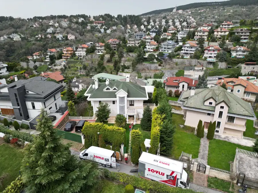 Ağaçlık bir yamaca yayılmış villalar ve bir villanın önünde yükleme yapan Soylu kamyonu ile panelvanı, havadan