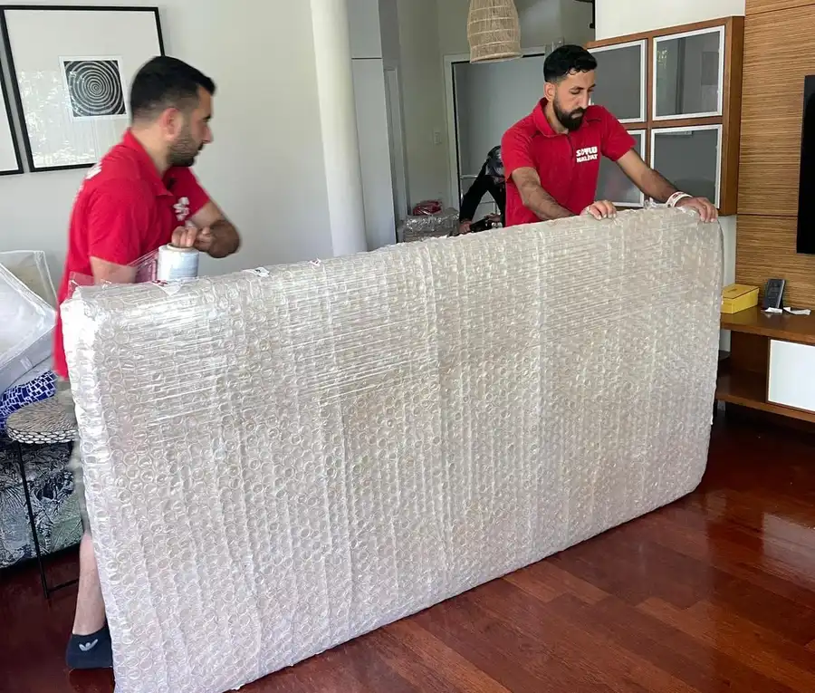 Salonda bir yatağı balonlu naylon ve streç filmle saran iki Soylu çalışanı